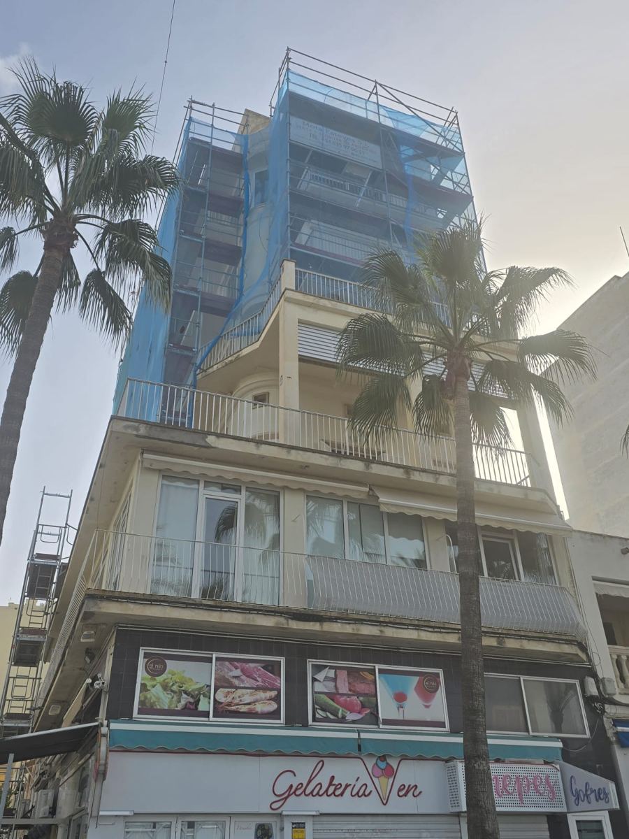 Edificio en paseo con palmeras y andamio en plantas altas
